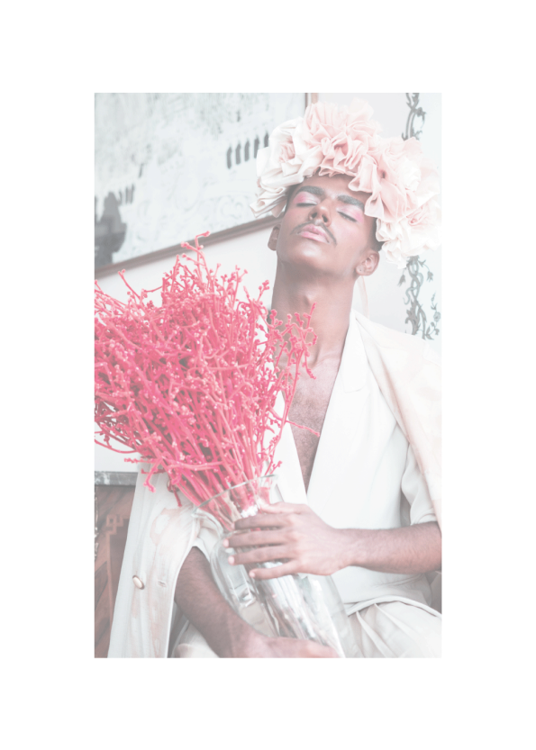 Indisk mand klædt i hvidt og makeup der holder en vase med lyserøde blomster.