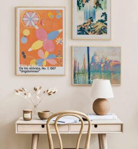 3 farverige billeder i ramme på væg med sandfarvet bord og skrivebord.